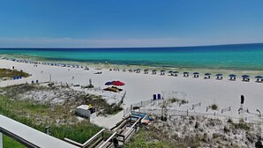 Ein Strand mit weißem Sand, einer Holzpromenade und einem wolkenlosen, blauen Himmel.