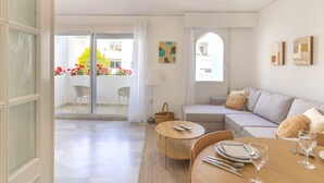 Een moderne woonkamer met een bank, eettafel en stoelen. Er is een balkon met uitzicht op een tuin.