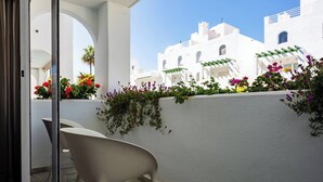 Een balkon met een witte stoel, een witte muur met planten en witte gebouwen op de achtergrond.