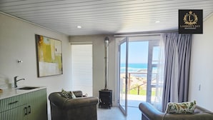 A modern living room with a view of the ocean, a fireplace, and a dining area with a green cabinet. - Lambert's Bay Beachfront (Lambert's Bay)