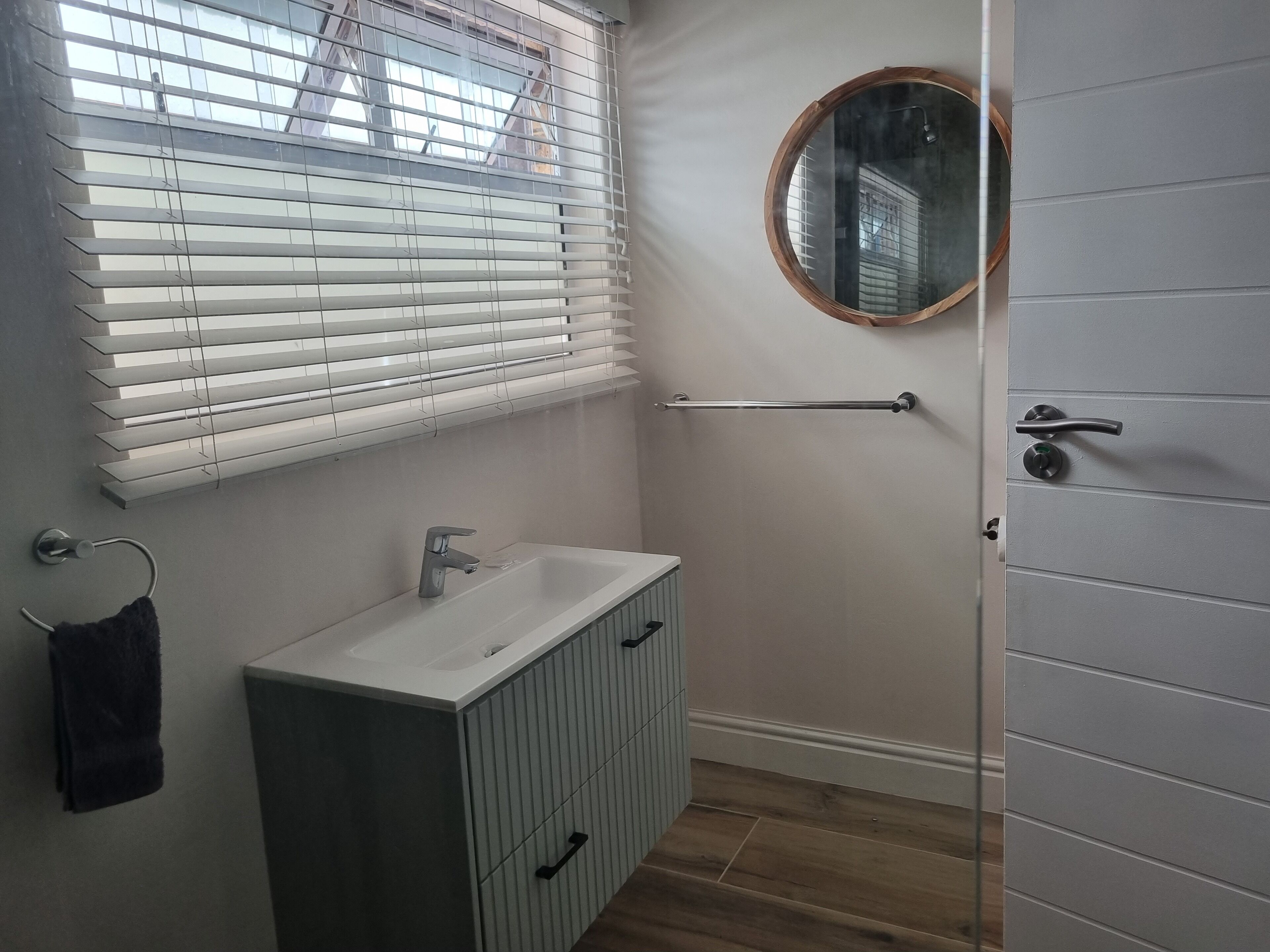 A bathroom with a white sink, a mirror, and a window with blinds.