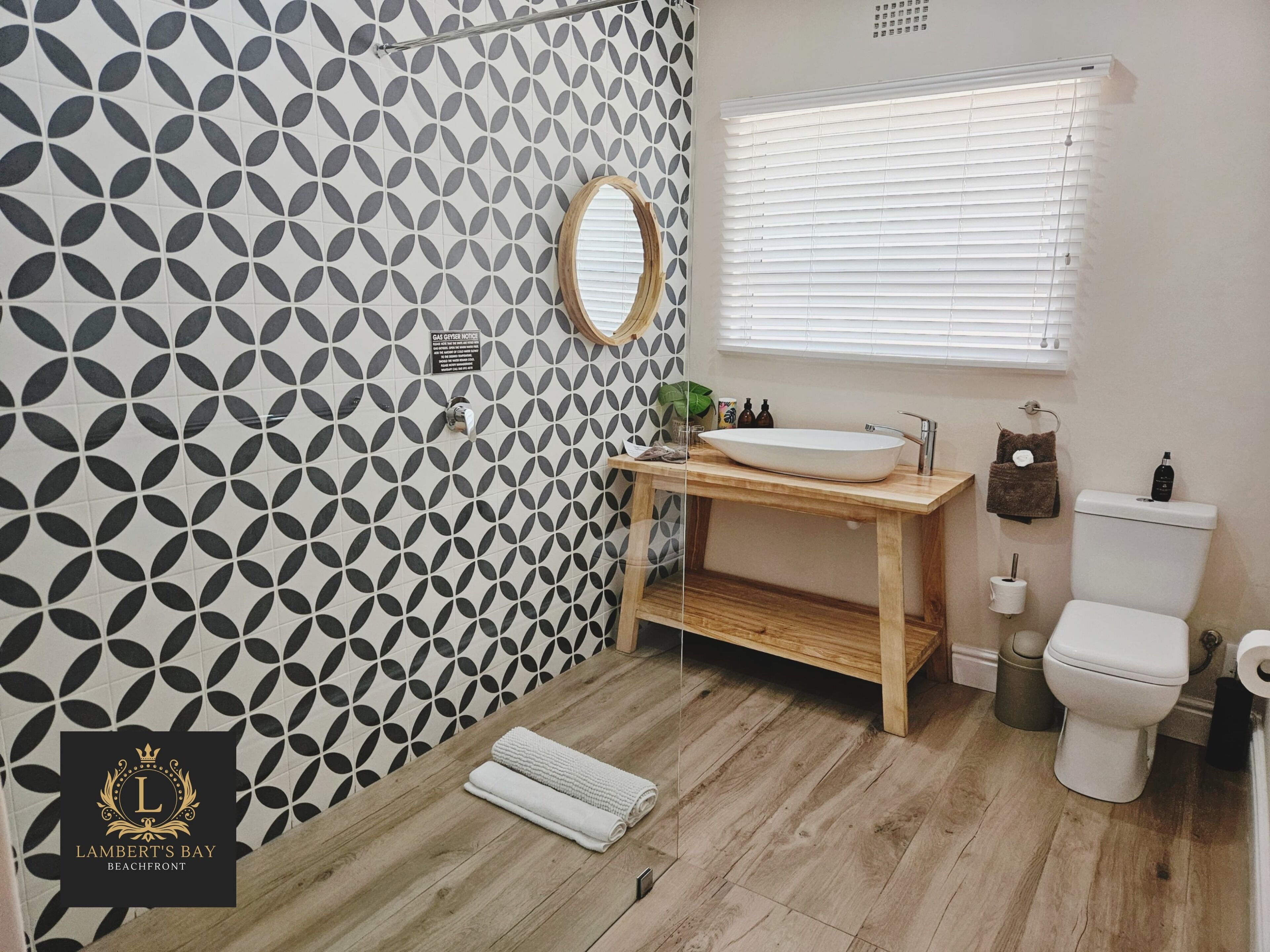 A bathroom with a geometric tile pattern, a wooden vanity, a sink, a toilet, and a window with blinds.