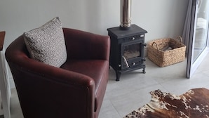 A living room with a red leather sofa, a patterned throw pillow, a black wood-burning stove, a woven basket, and a cowhide rug. - Lambert's Bay Beachfront (Lambert's Bay)