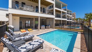 A multi-story hotel with a pool area, including sun loungers and a covered seating area. - Luxury 6-Bedroom Retreat | Pool & Beach Access (Gulf Shores)