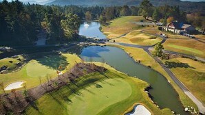 A golf course with a pond, a clubhouse, and a view of the surrounding hills. - Spacious mountain getaway on golf course, near trails, waterfalls & breweries! (Laurel Park)