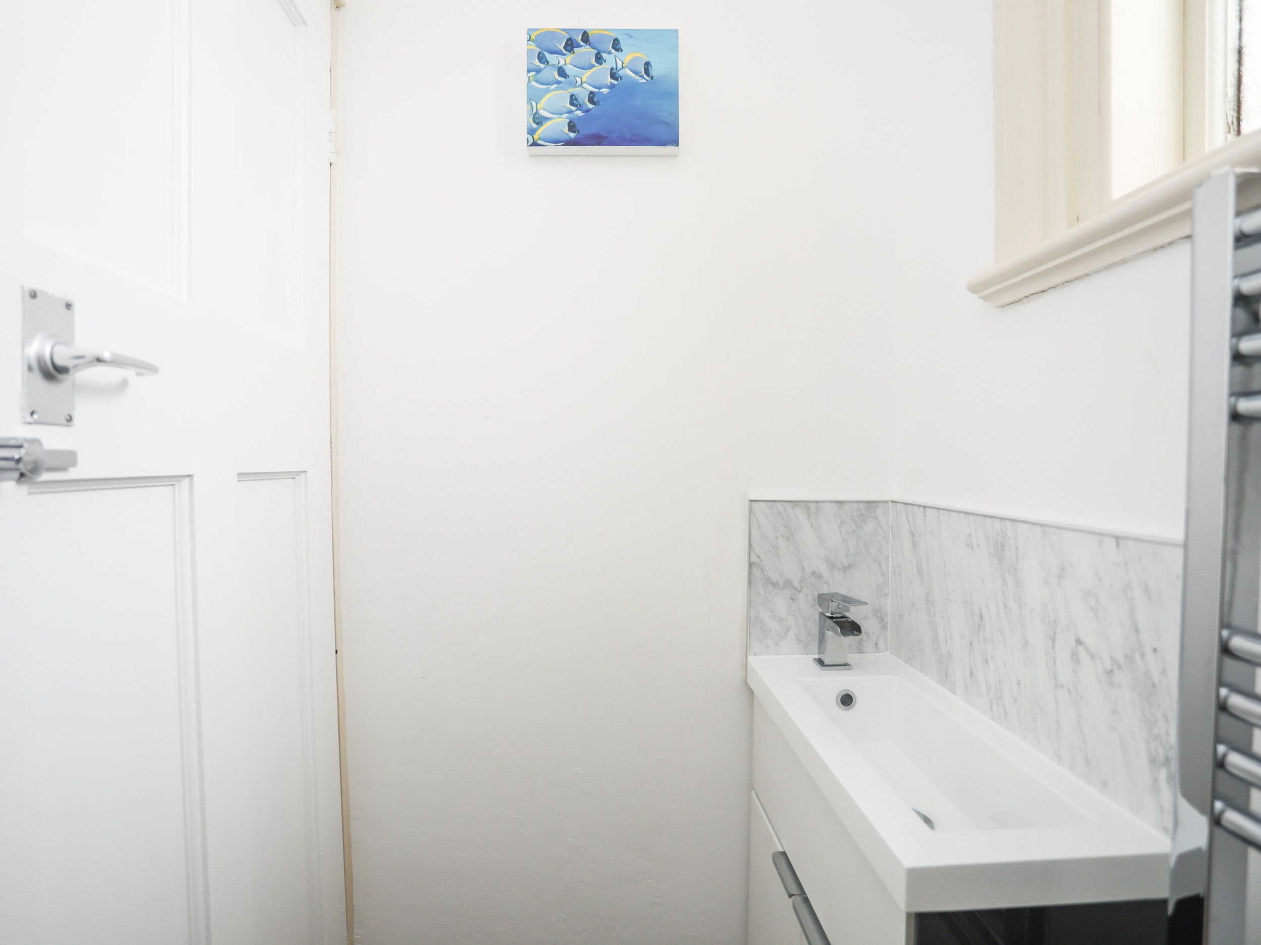 Un baño con una puerta blanca, un lavamanos de mármol y un pequeño cuadro en la pared.