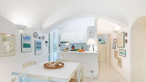 A bright, open-plan kitchen and dining area with white cabinetry, a central island with fruit and a lamp, and framed artwork on the walls.