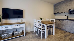 Eine moderne Küche mit Holztisch, weißen Stühlen, einem Flachbildfernseher und grauen Schränken.