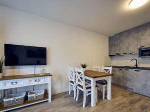 Una cocina moderna con una mesa de comedor de madera, sillas blancas, un televisor de pantalla plana y armarios grises.