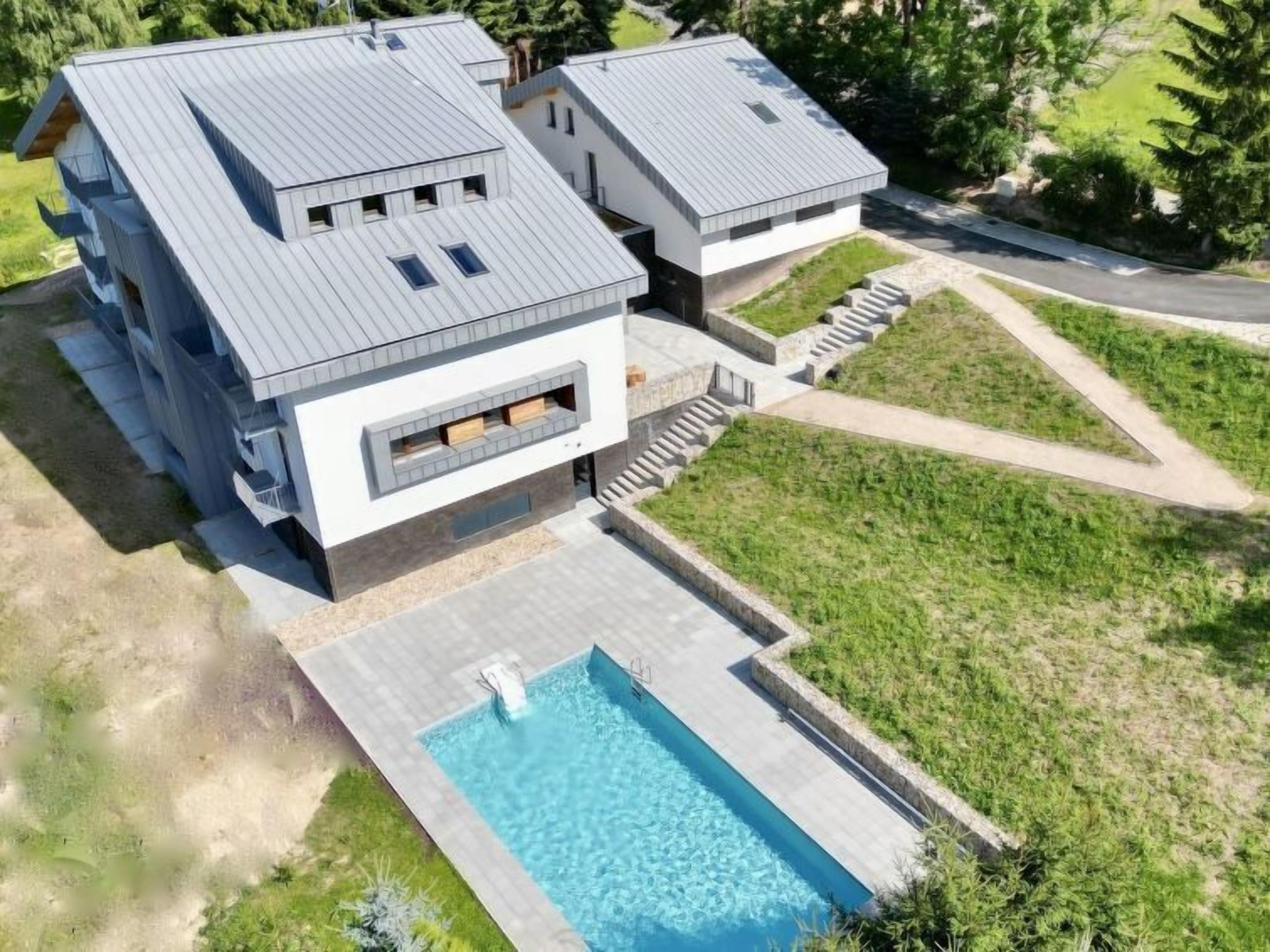 A modern two-story house with a swimming pool, a driveway, and a well-maintained lawn.