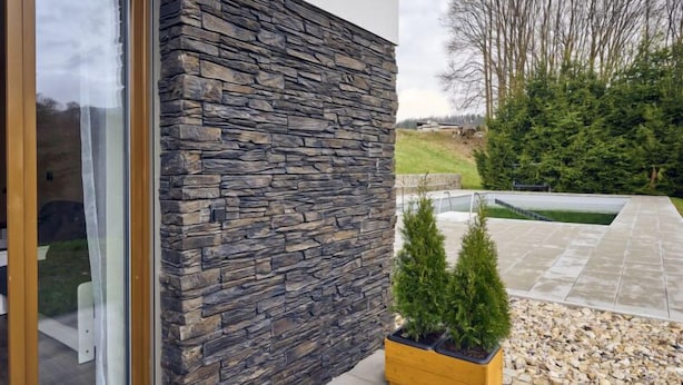 Ein modernes Gebäude mit Natursteinfassade, Glastür und einem kleinen Garten mit Pool und Kübelpflanzen.