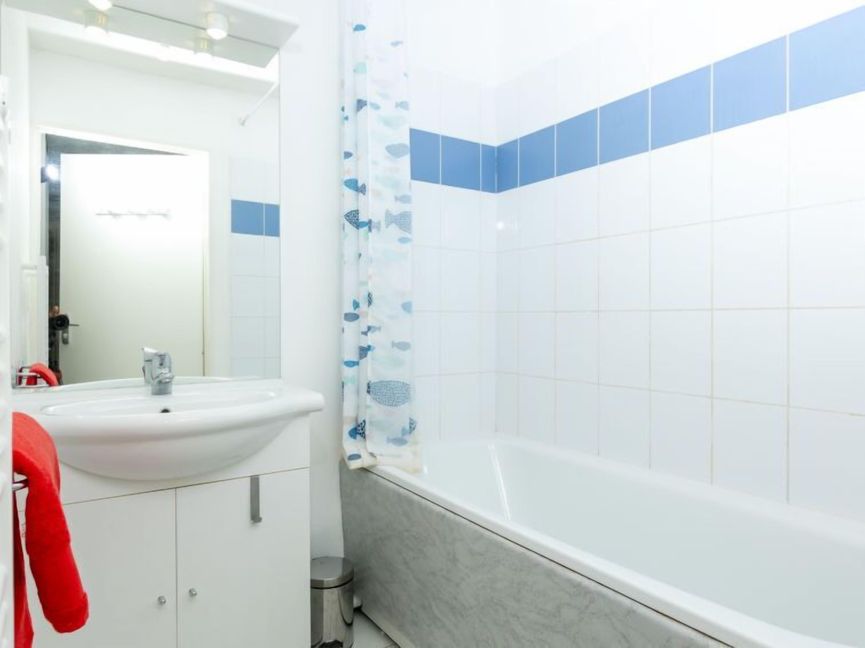 Une salle de bain avec un lavabo blanc, un miroir, une baignoire et des murs recouverts de carreaux bleus.