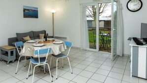 A dining area with a table set for four, a sofa, a lamp, and a view of the backyard through a glass door. - Les Caps Horniers by Interhome (Pleurtuit)