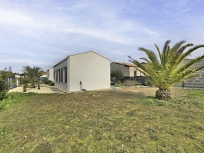 Um edifício moderno com telhado plano, entrada com calçada pavimentada e gramado bem cuidado com palmeiras.