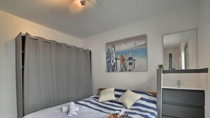 Una camera da letto con un letto, un quadro con tavole da surf, un bagno con uno specchio e un vassoio con arance sul letto.