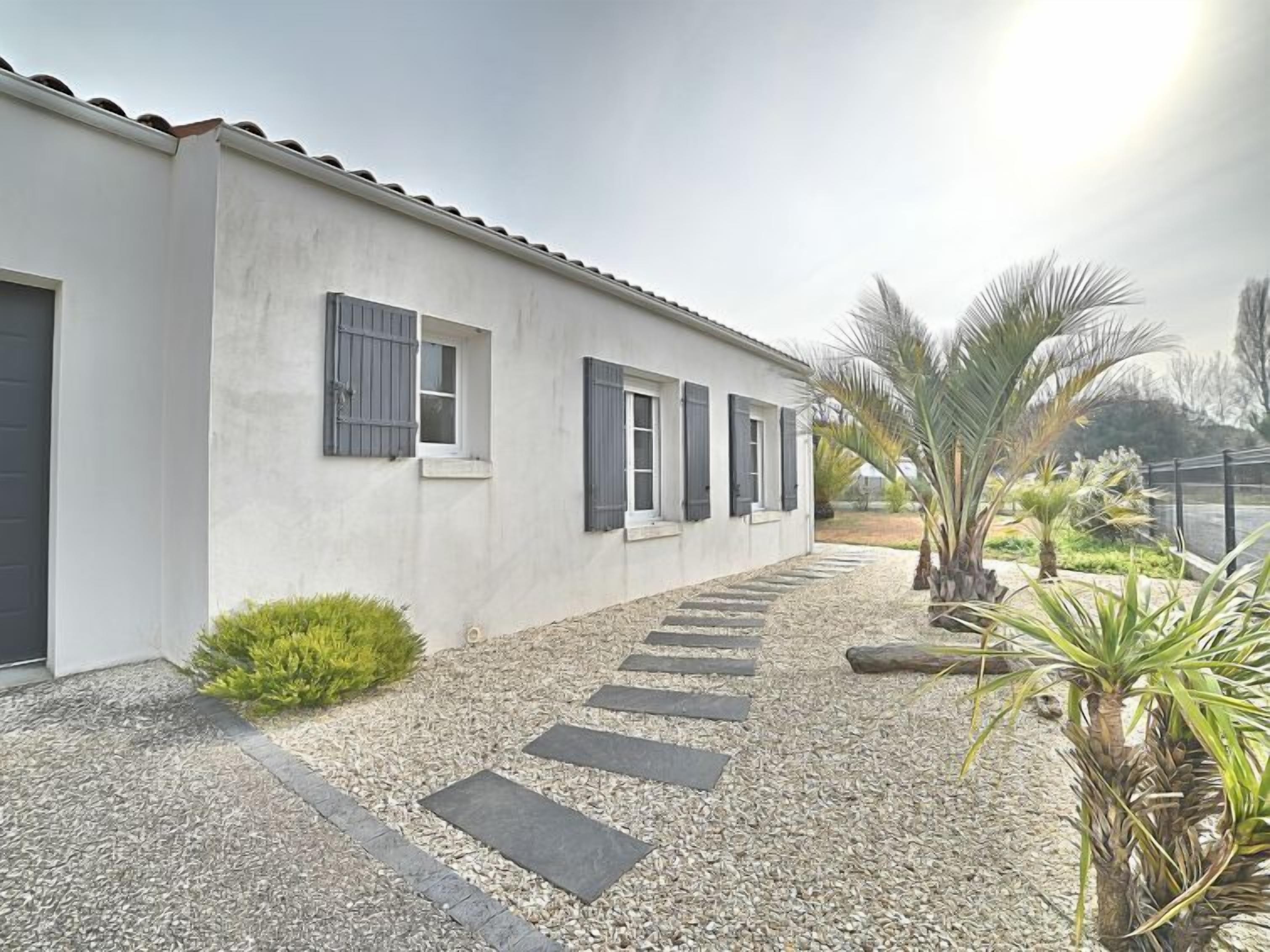 A modern building with a white facade, dark shutters, and a gravel pathway leading to the entrance.