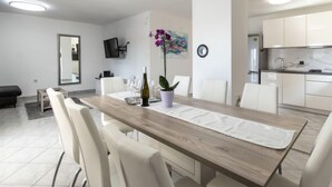 Un espace repas moderne avec une table en bois, des chaises blanches et une cuisine en arrière-plan.