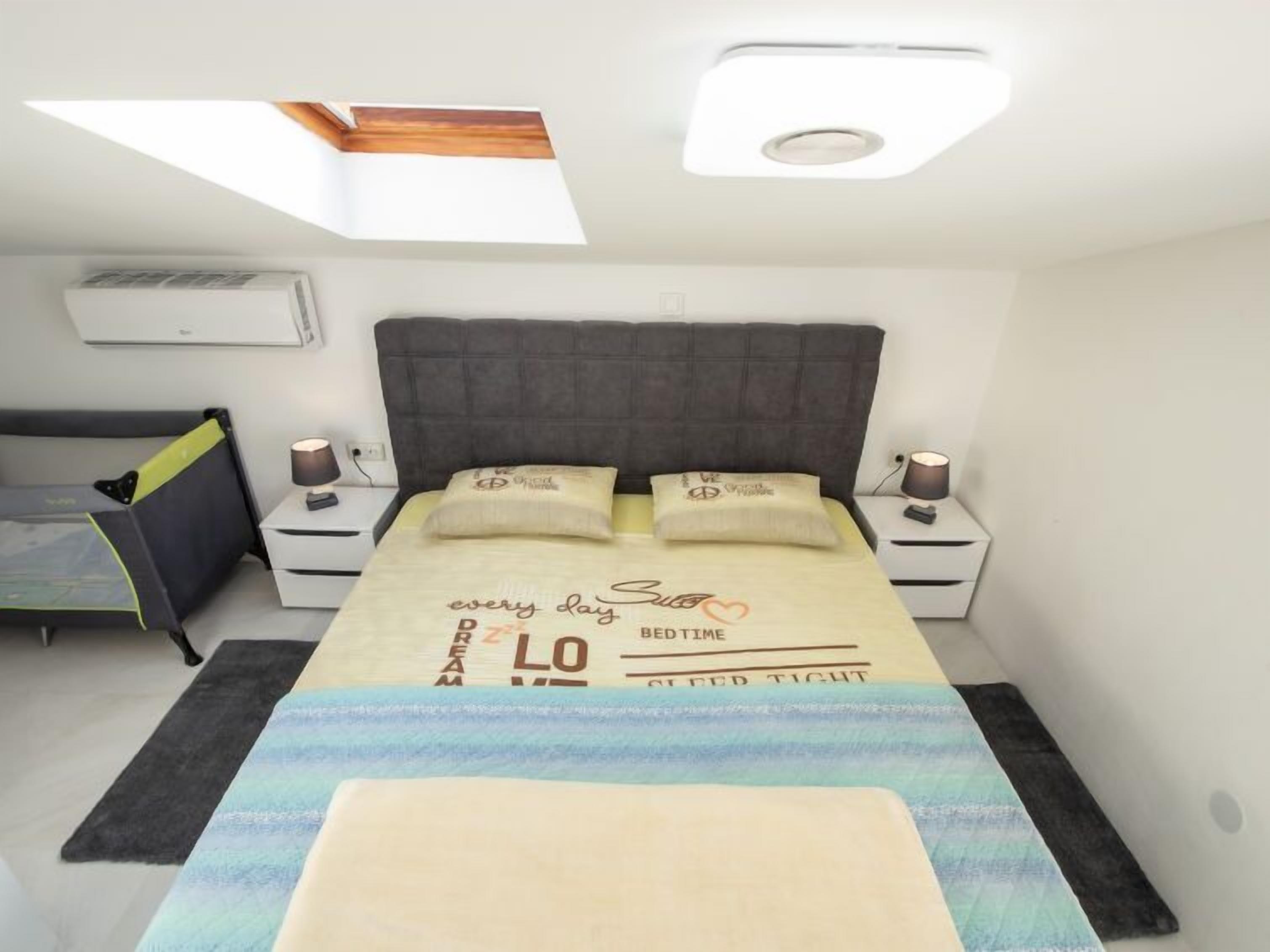 Un dormitorio con una cama, dos mesitas de noche, un escritorio y una lámpara en el techo.