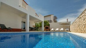 Une piscine à l’eau d’un bleu cristallin, entourée d’un bâtiment blanc dont l’un des côtés est bordé d’un mur de pierre.