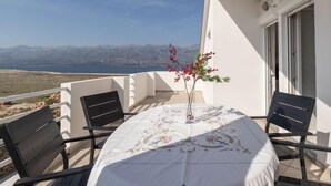 Un balcon avec une table dressée pour deux personnes, un vase rempli de fleurs et une vue sur la mer et les montagnes.