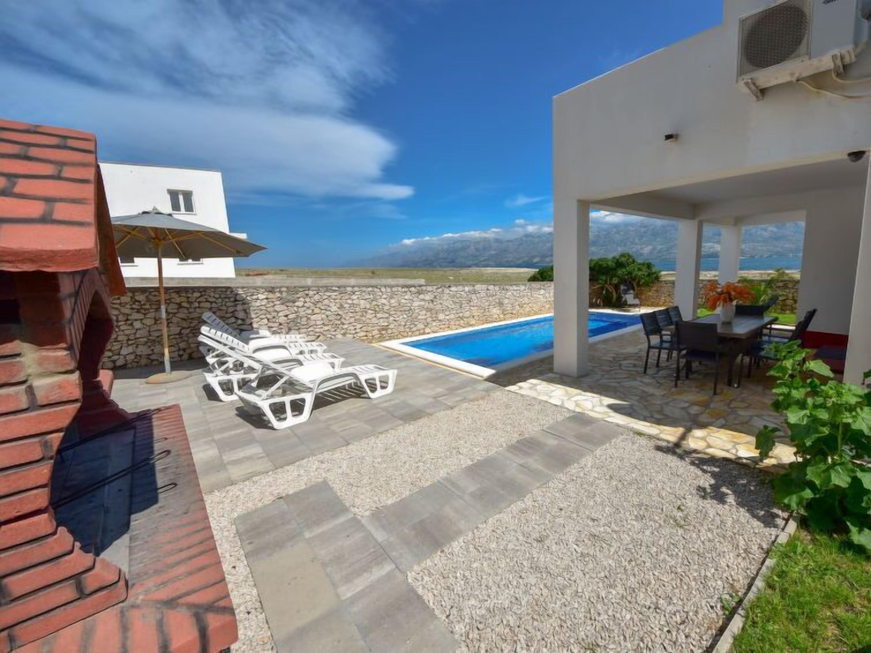 Un espace aménagé au bord de la piscine, avec une terrasse en pierre, des chaises longues et une vue sur la mer.