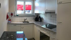 Una cocina compacta con armarios blancos, encimera de granito, horno empotrado y ventana con persianas rojas.