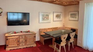 Un comedor con una mesa y sillas de madera, un mueble con cajones y un televisor de pantalla plana montado en la pared.