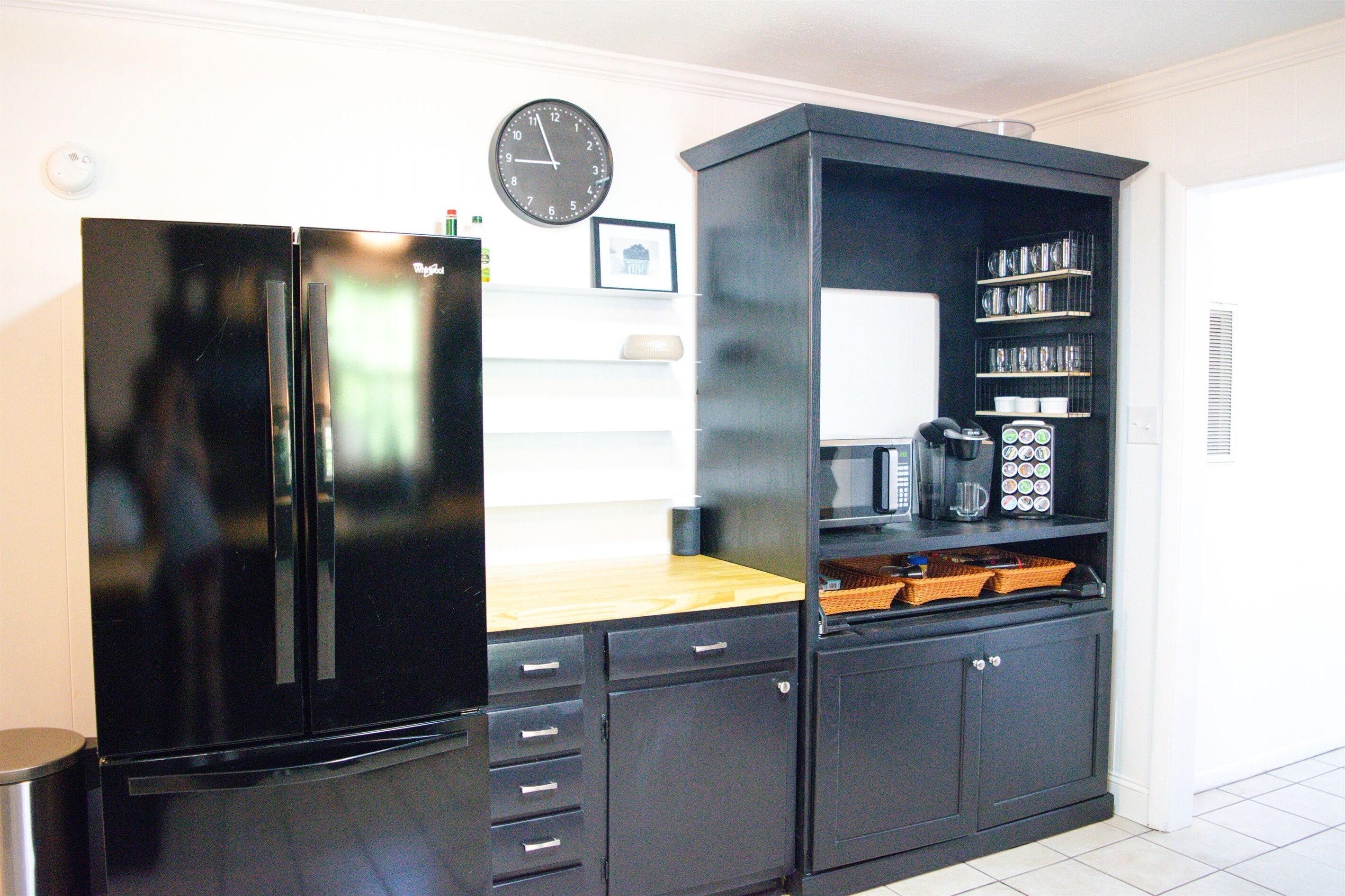 A kitchen with a black refrigerator, a microwave, and a clock on the wall.