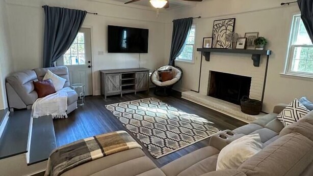 Ein Wohnzimmer mit einer Couch, einem Couchtisch, einem Kamin, einem Deckenventilator und einem an der Wand befestigten Fernseher.