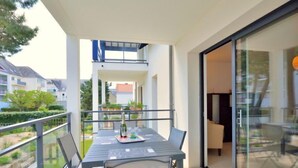 Un balcon avec une table et des chaises, donnant sur un jardin et les bâtiments voisins.