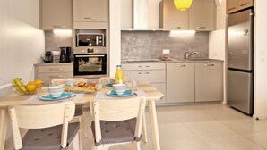 Une cuisine moderne avec un coin repas, dotée de meubles de couleur claire, d’appareils électroménagers en acier inoxydable et d’un luminaire suspendu jaune.