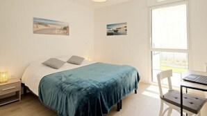 Une chambre avec un lit, un bureau et une chaise. Il y a deux tableaux accrochés au mur.