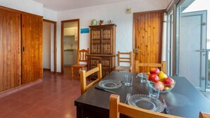 Un coin repas avec une table en bois foncé, quatre chaises et un panier de fruits. On y trouve également un buffet en bois et une porte qui donne sur une autre pièce.