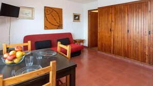 Un coin repas avec une table dressée pour deux personnes, un canapé rouge et une armoire en bois.