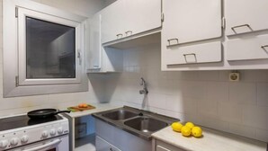 Une cuisine de taille réduite avec des meubles blancs, une cuisinière, un évier et une fenêtre.