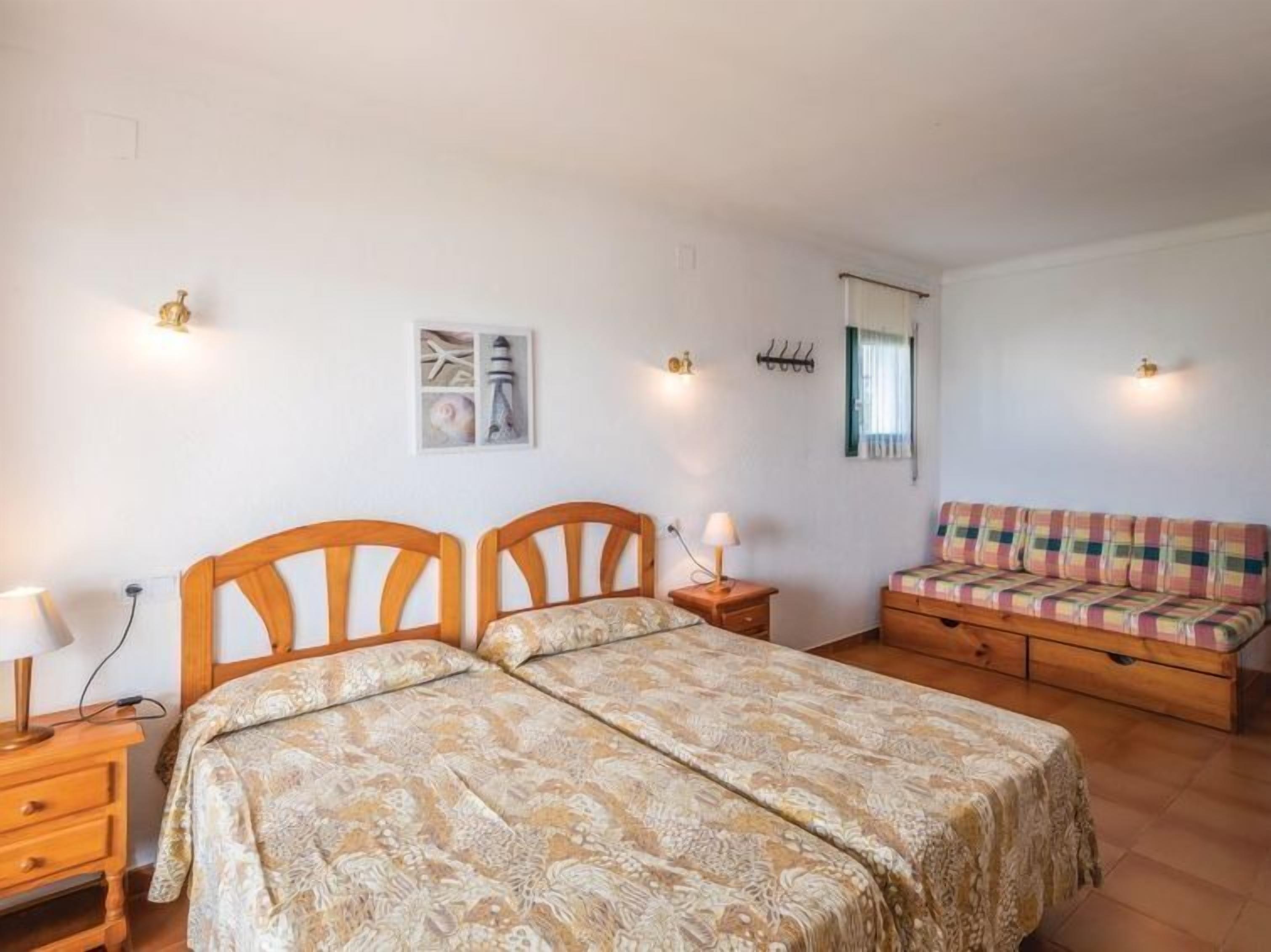 Une chambre à coucher avec un lit double, un canapé, une table de chevet avec une lampe, un miroir fixé au mur et un tableau encadré.