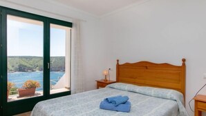 Ein Schlafzimmer mit einem Bett, einem Nachttisch, einem Fenster mit Meerblick und einer Zimmerpflanze.