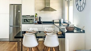 Una cocina moderna con armarios blancos, un refrigerador de acero inoxidable, horno empotrado y un reloj de pared grande.
