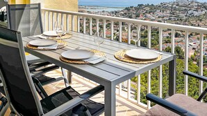 Un balcón con una mesa dispuesta para dos personas, con vista a un pueblo costero.