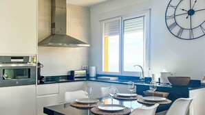 Una cocina moderna con un ventanal grande, un reloj en la pared y una zona de comedor con mesa puesta para cuatro.