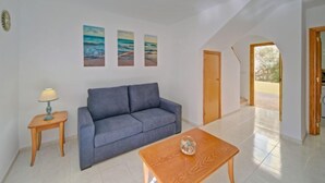 A living room with a sofa, a coffee table, a lamp, and three paintings on the wall.