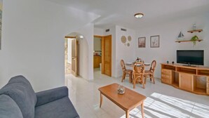 A living room with a sofa, a coffee table, a TV, and a dining area with chairs and a table.
