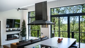 Eine moderne Küche mit einer zentralen Kochinsel, einem Einbauherd und einem großen Fenster mit Blick auf einen Wald.