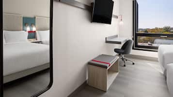 Een moderne hotelkamer met een bed, een bureau, een stoel en een groot raam met uitzicht over de stad.