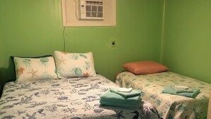 Une chambre avec deux lits, dont un plus grand et un plus petit, tous deux dotés de draps à motifs floraux. On y trouve un ventilateur de plafond et un appareil de climatisation fixé au mur.
