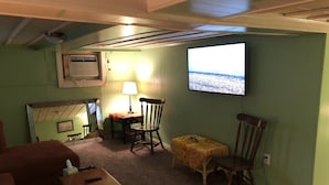 Une pièce confortable avec un téléviseur fixé au mur, une petite table avec une lampe et deux chaises.
