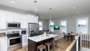 A modern kitchen with white cabinets, stainless steel appliances, a central island with stools, and a dining area with a table and chairs. - IN THE HEART OF DEWEY BEACH - 2002 Bayard Ave (Dewey Beach)