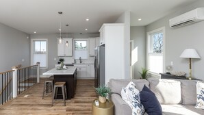 A modern kitchen with white cabinets, a central island, and a dining area. There is a staircase leading to an upper level. - IN THE HEART OF DEWEY BEACH - 2002 Bayard Ave (Dewey Beach)
