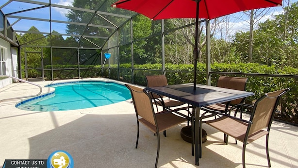 A covered outdoor pool area with a table and chairs, surrounded by a glass enclosure. - Modest Charmer W/ Private Pool (Clermont)