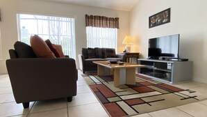 A living room with a sofa, a coffee table, a TV, and a lamp. - Modest Charmer W/ Private Pool (Clermont)